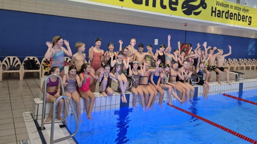Grote groep deelnemers in zwemkleding aan de rand van een binnenzwembad