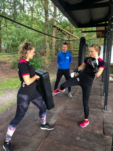 2 vrouwen doen de activiteit boksfit onder begeleiding van een instructeur