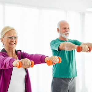 Een mevrouw en een meneer die hun armen voor zich uitstrekken met een gewichtje in beide handen.