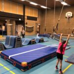 Kind die aan trapeze gaat zwaaien in gymzaal met verschillende matten op de vloer