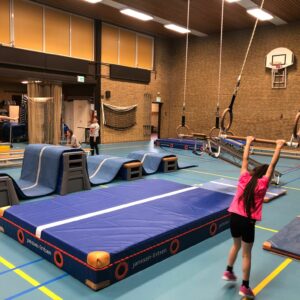Kind die aan trapeze gaat zwaaien in gymzaal met verschillende matten op de vloer