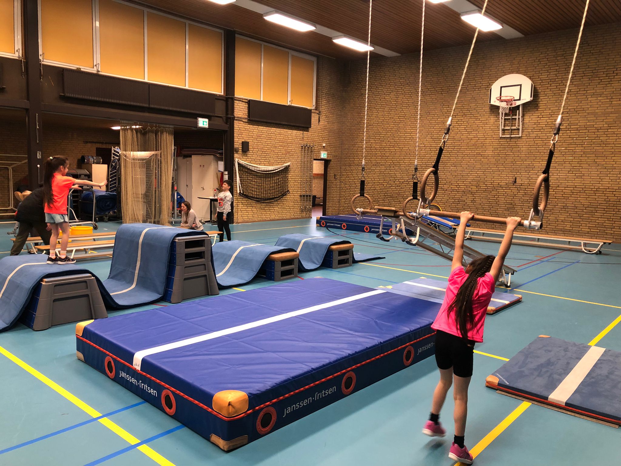 Kind die aan trapeze gaat zwaaien in gymzaal met verschillende matten op de vloer