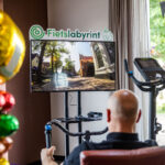 Kalende man fiets een virtuele route op televisie vanuit stoel in huiskamer