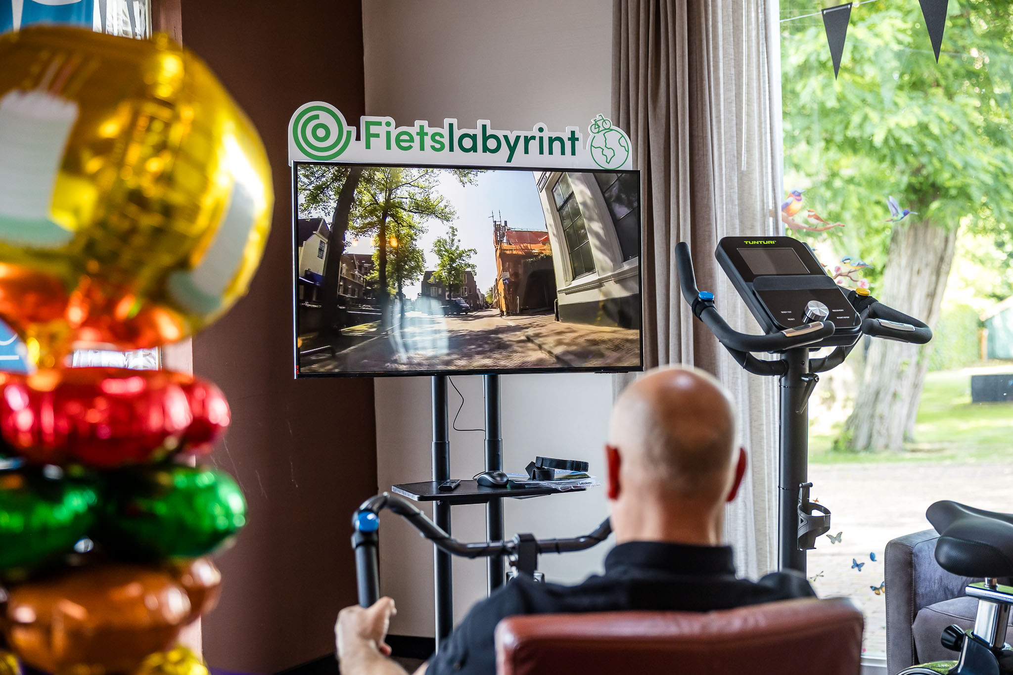 Kalende man fiets een virtuele route op televisie vanuit stoel in huiskamer