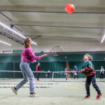 Ouder met tennisracket die samen met kind met racket ballon hoog probeert te houden