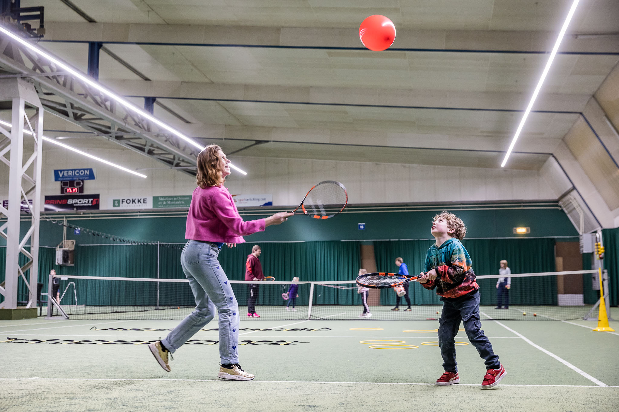 Ouder met tennisracket die samen met kind met racket ballon hoog probeert te houden