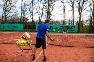 Meerdere kinderen op een tennisbaan krijgen trainingen van een tennisleraar