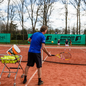 Meerdere kinderen op een tennisbaan krijgen trainingen van een tennisleraar