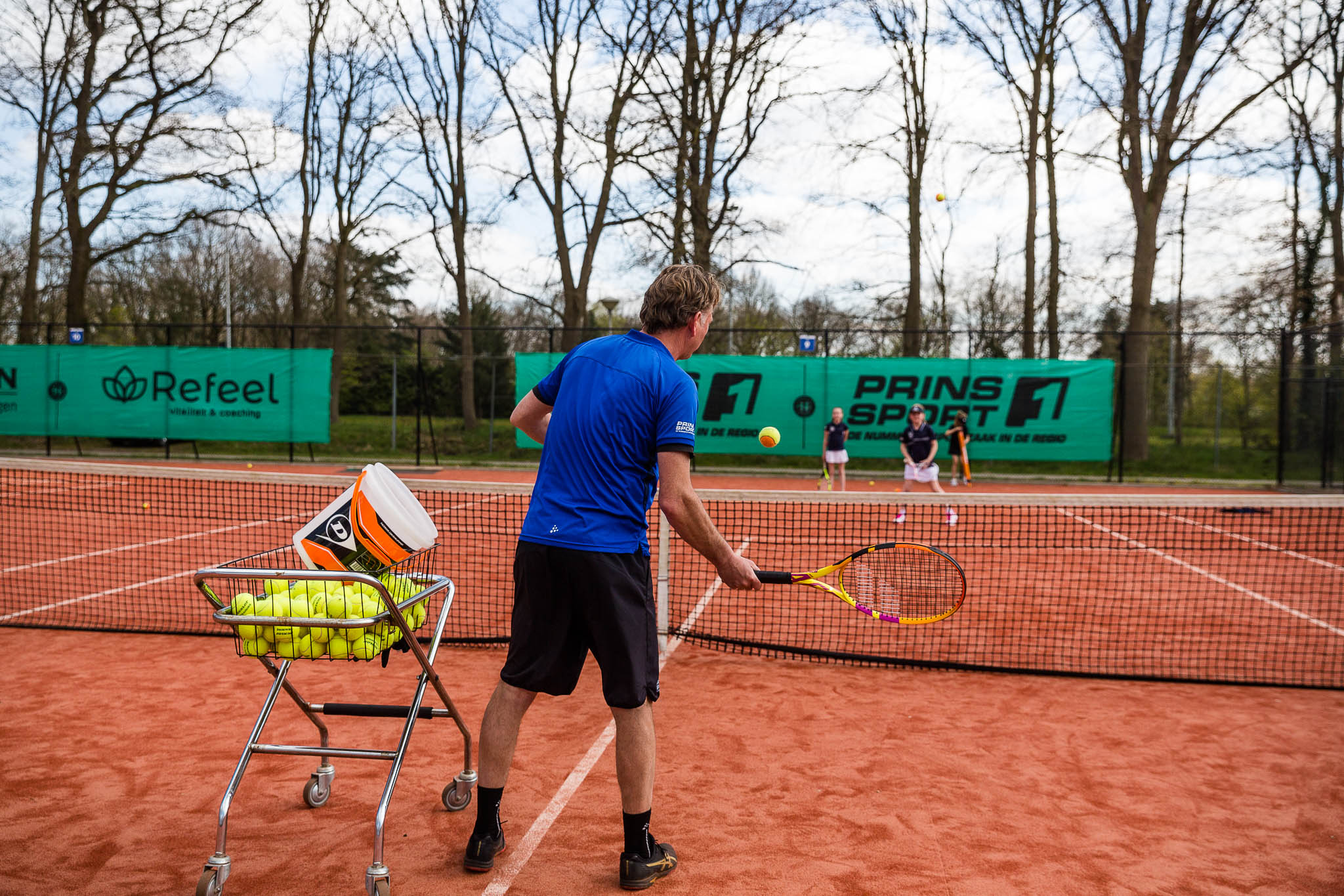 Meerdere kinderen op een tennisbaan krijgen trainingen van een tennisleraar
