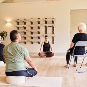 Meerdere mensen een les stoelyoga volgen onder begeleiding van een yoga instructeur