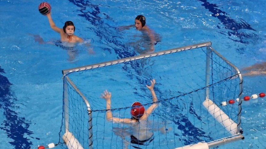 3 waterpolo spelers waarbij 1 speler de bal gaat gooien richting waterpolo doel